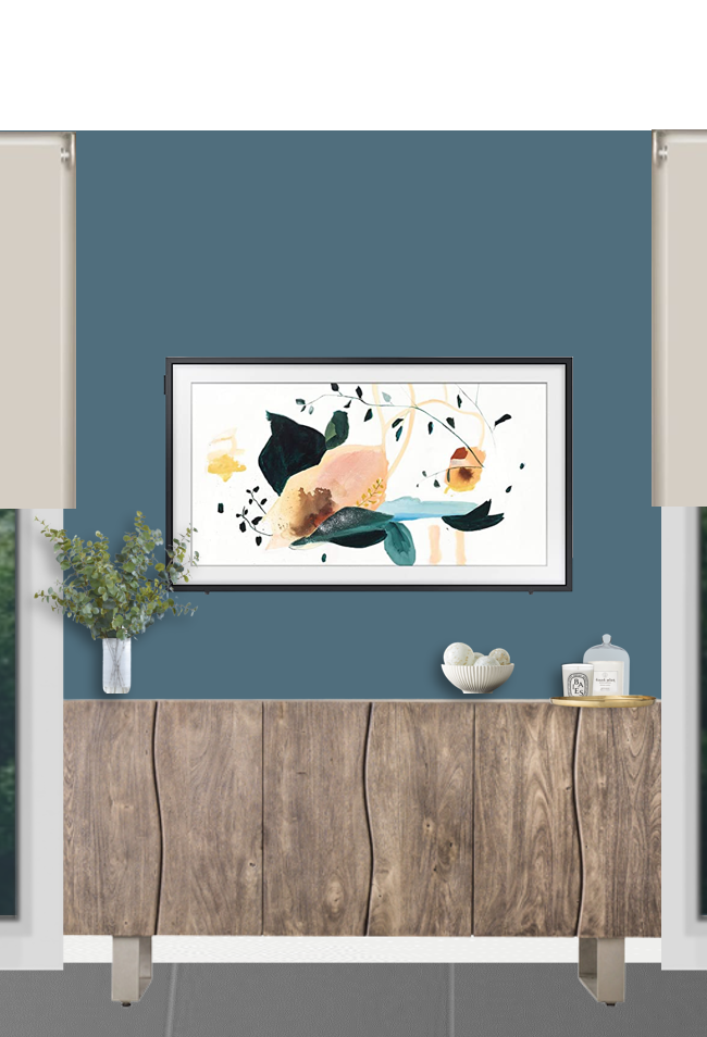 Interior of a room with a blue wall, a wooden sideboard, a vase with greenery, and a framed abstract art piece