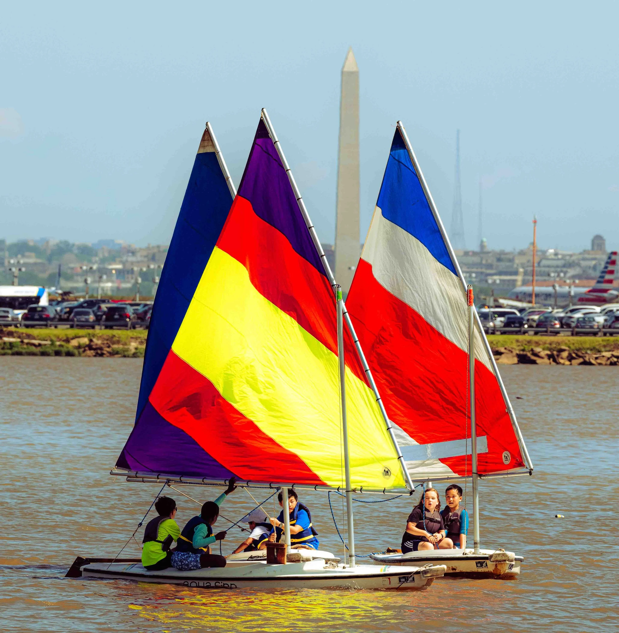 Brightly colored sails fill the river as young sailors develop confidence and technical skills.
