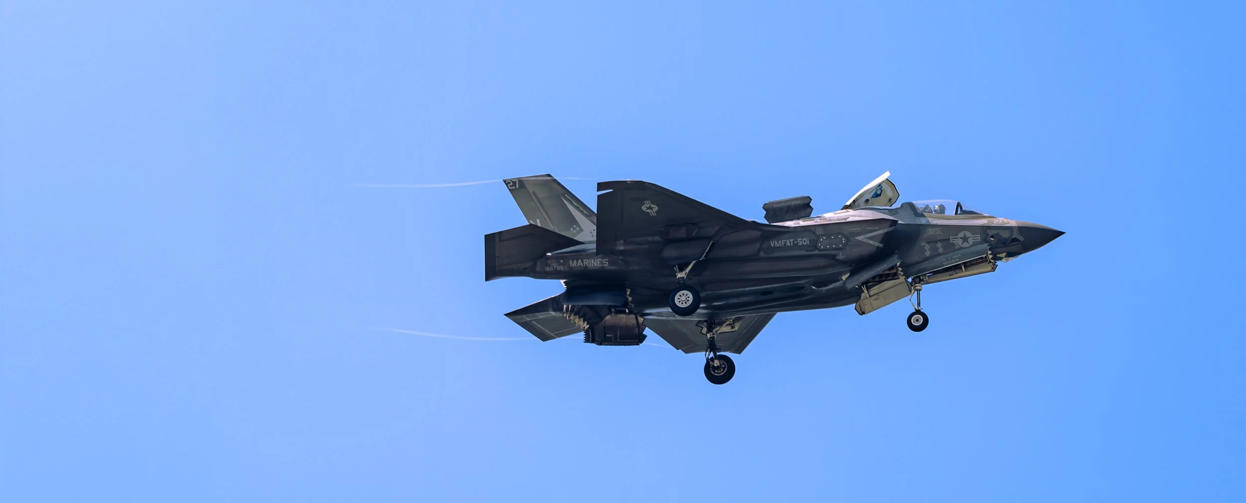 An F-35 Lightning II prepares for a demonstration pass with landing gear extended against a clear blue sky.