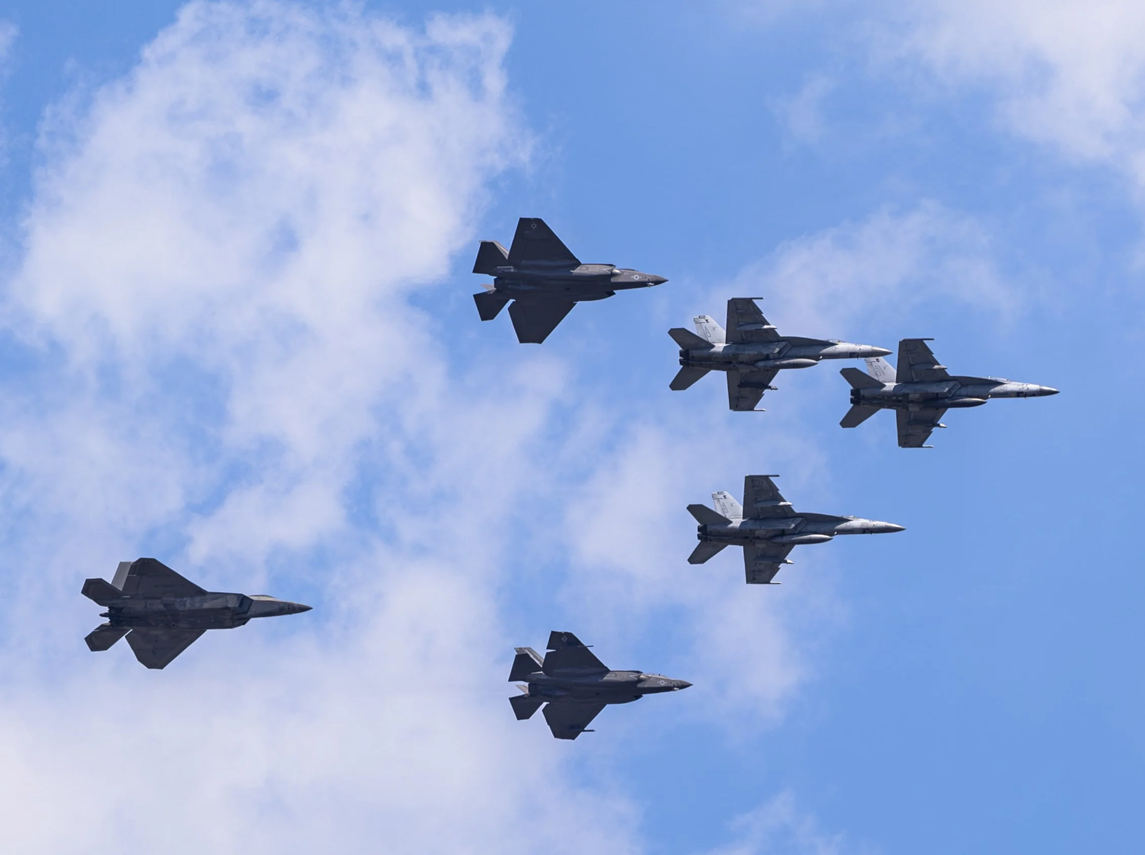 A mixed formation of F-35 Lightning II fighters flies through scattered clouds during the historic military flyover.