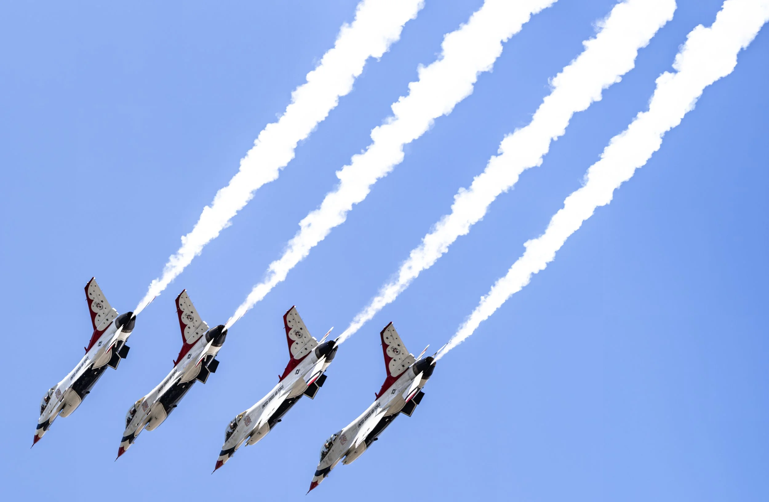 The Thunderbirds climb in tight formation, leaving bright white smoke trails that cut across the summer sky.