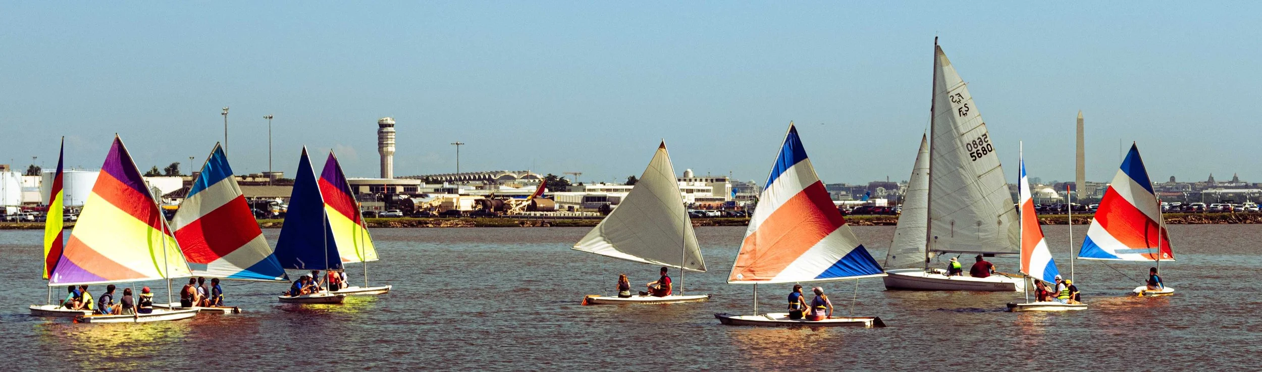 Student sailors practice sail trim and steering in open water near the Washington shoreline.