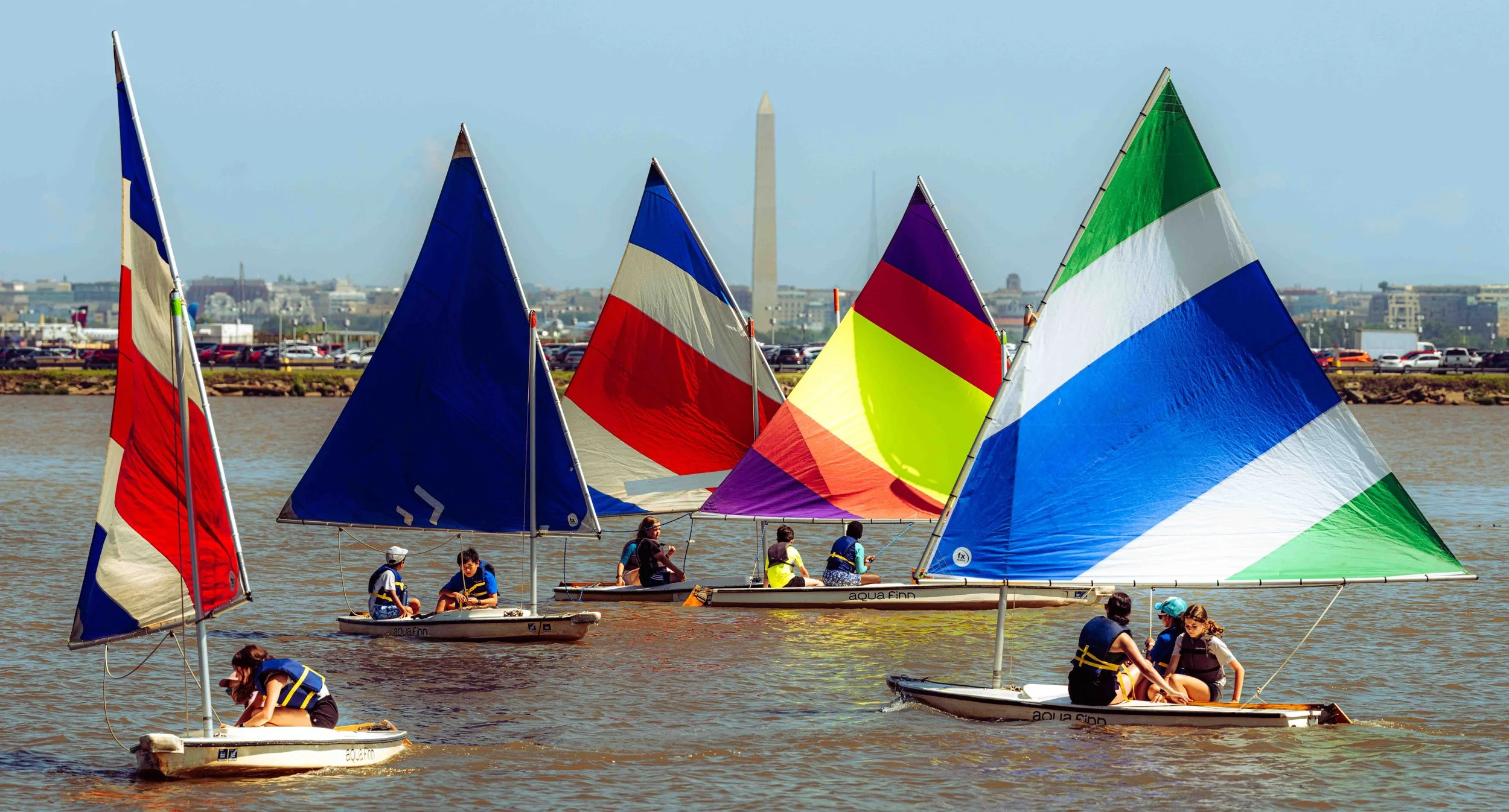 A fleet of brightly colored sails catches the wind during a Washington Sailing School training session.