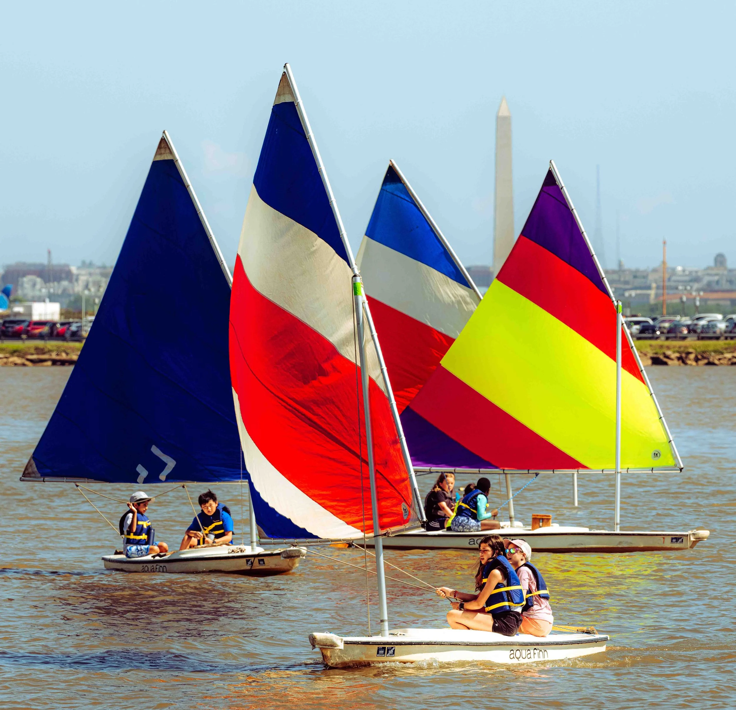 Colorful training boats sail in formation against the backdrop of the Washington skyline.
