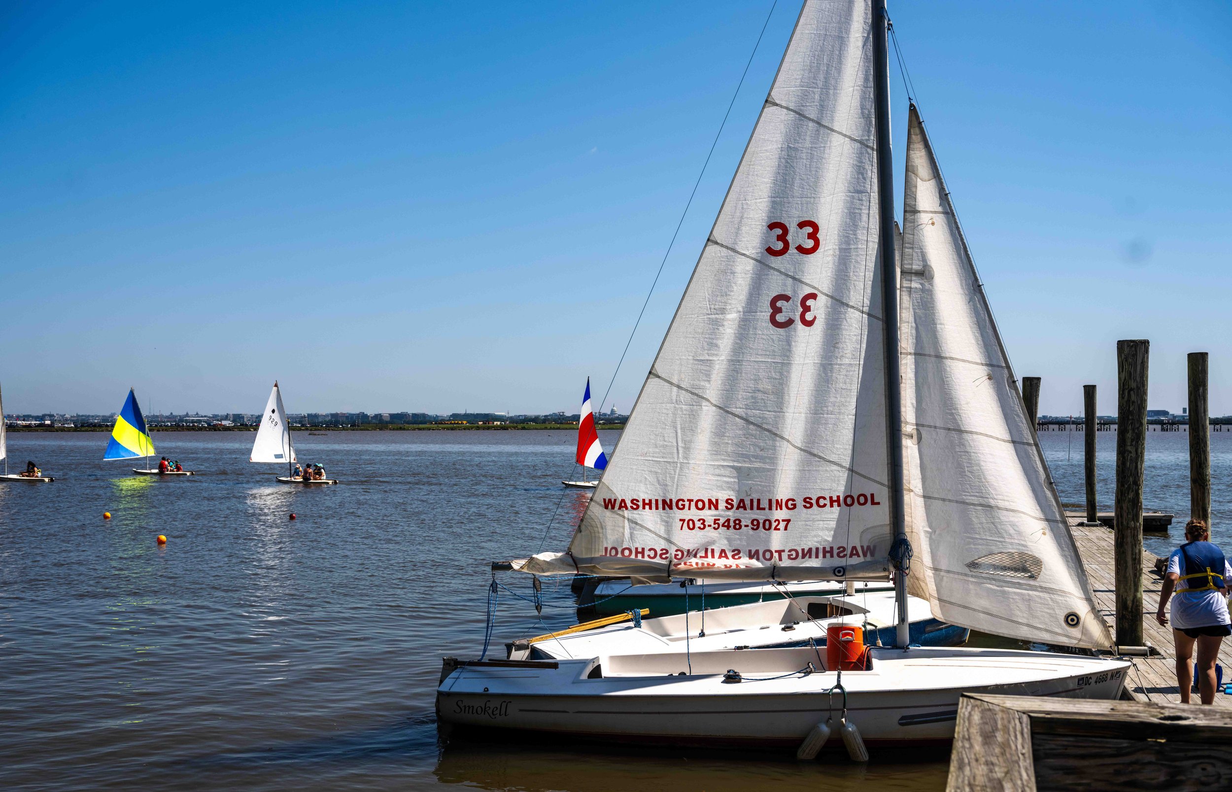 Student sailors prepare multiple boats for launch during a busy summer training session.
