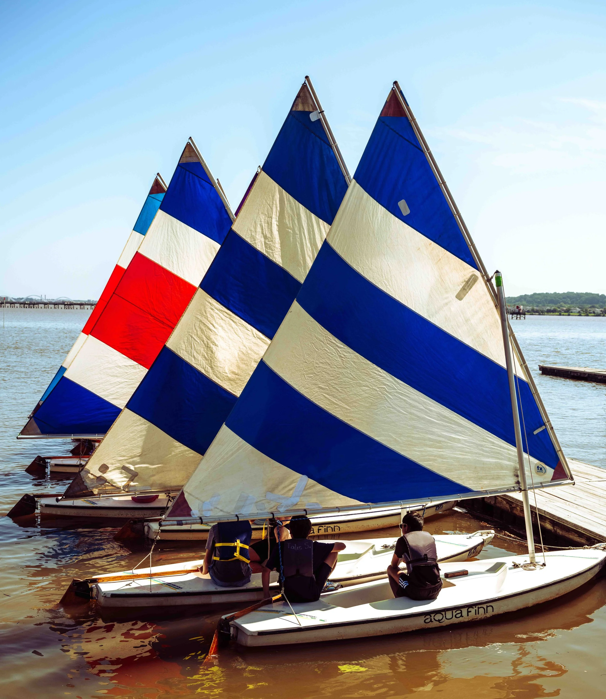 A fleet of youth sailing boats travels across calm waters near the nation's capital.
