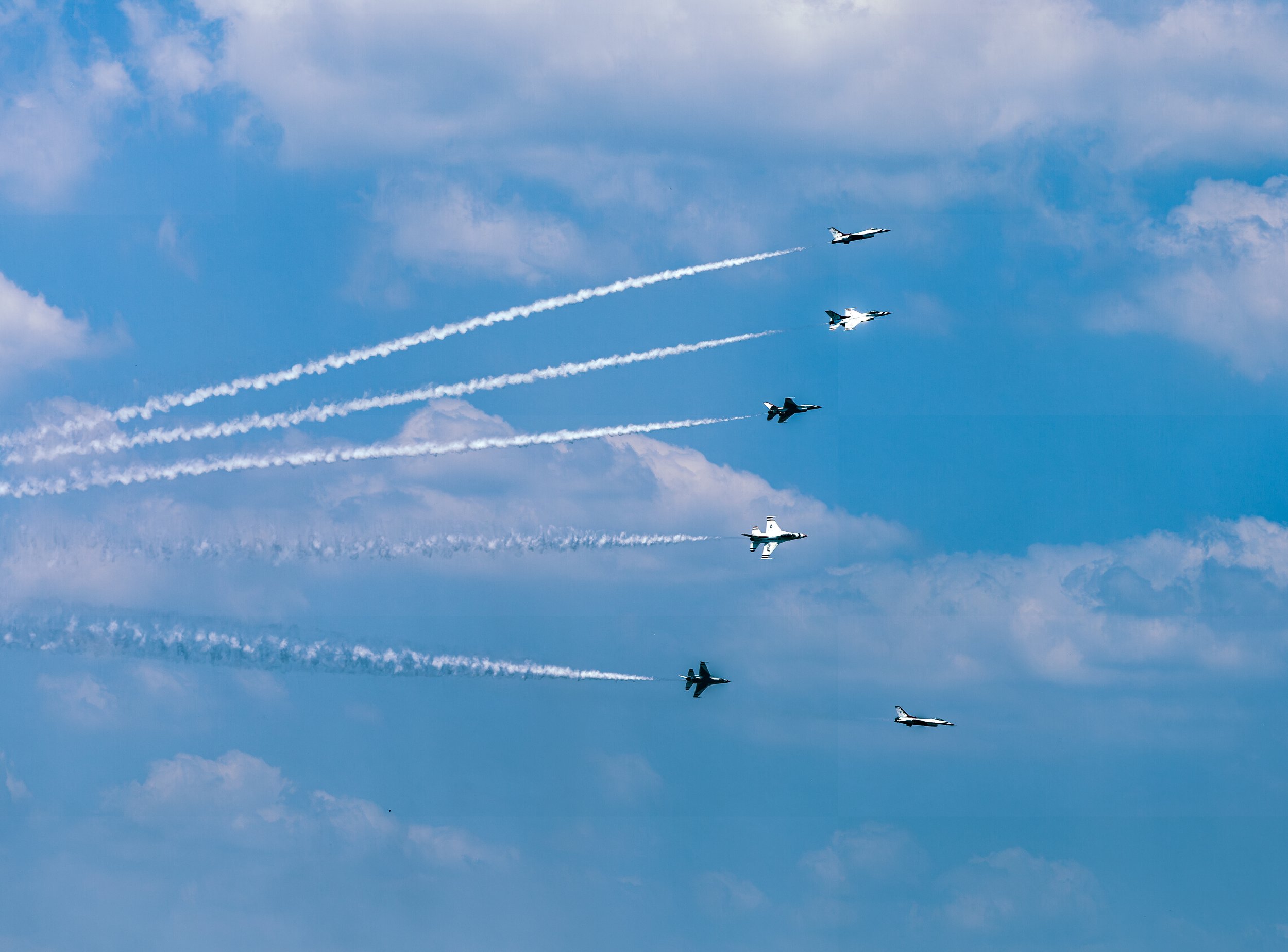 The Thunderbirds perform a precision aerial maneuver, leaving long white smoke trails against a deep blue summer sky.