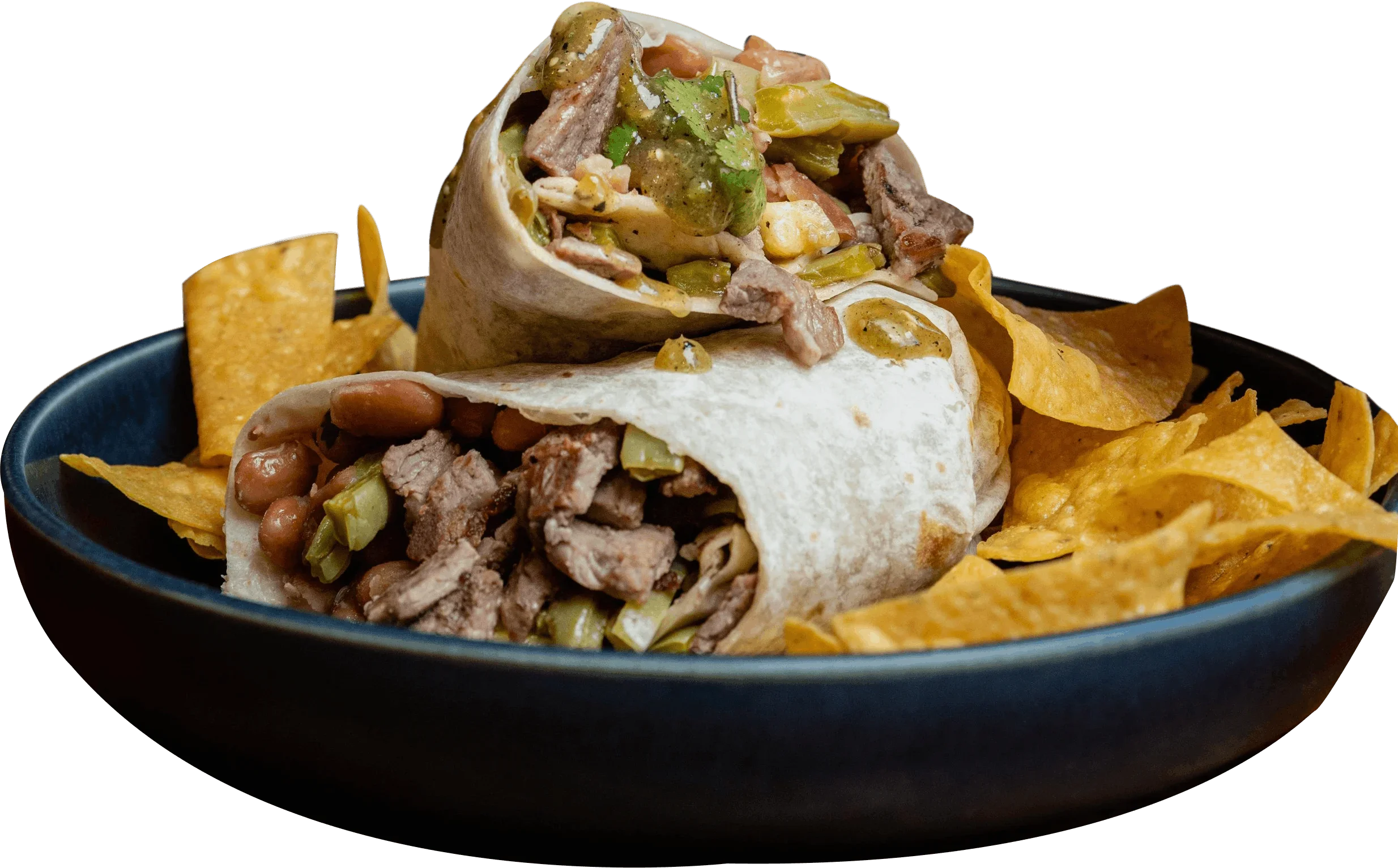 A black bowl filled with shredded beef, beans, and green chilies, topped with a soft flour tortilla and garnished with sauce, surrounded by yellow tortilla chips.