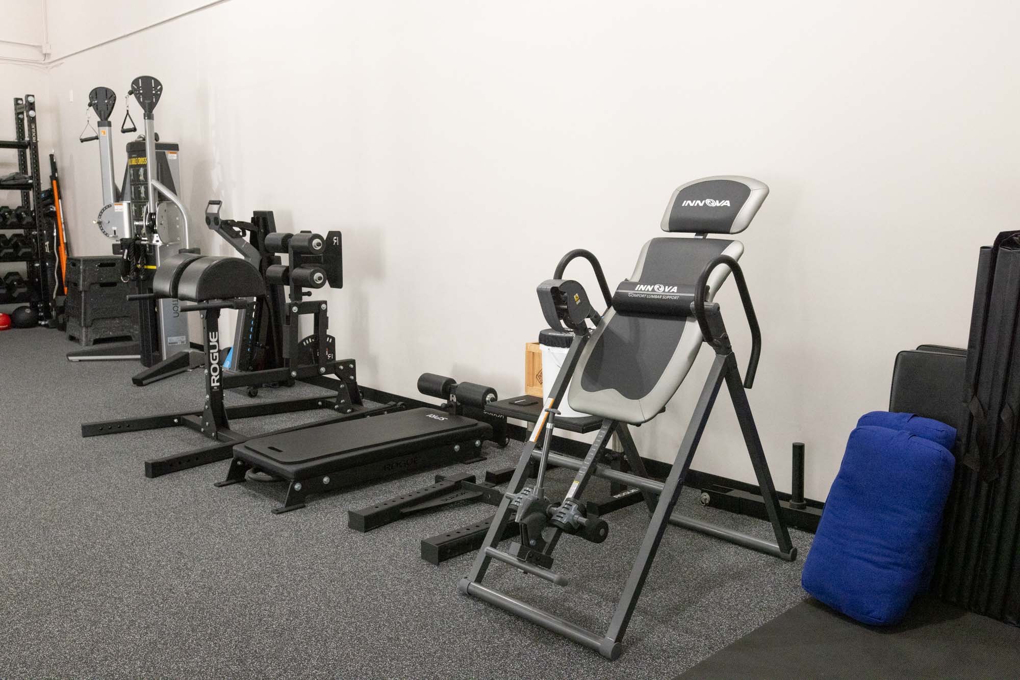 Resilient Body Gym interior with various fitness equipment, including an inversion table, rowing machine, and adjustable weight bench.