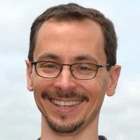 Nick Strauss-Klein. Man with short dark hair and glasses smiling outdoors.