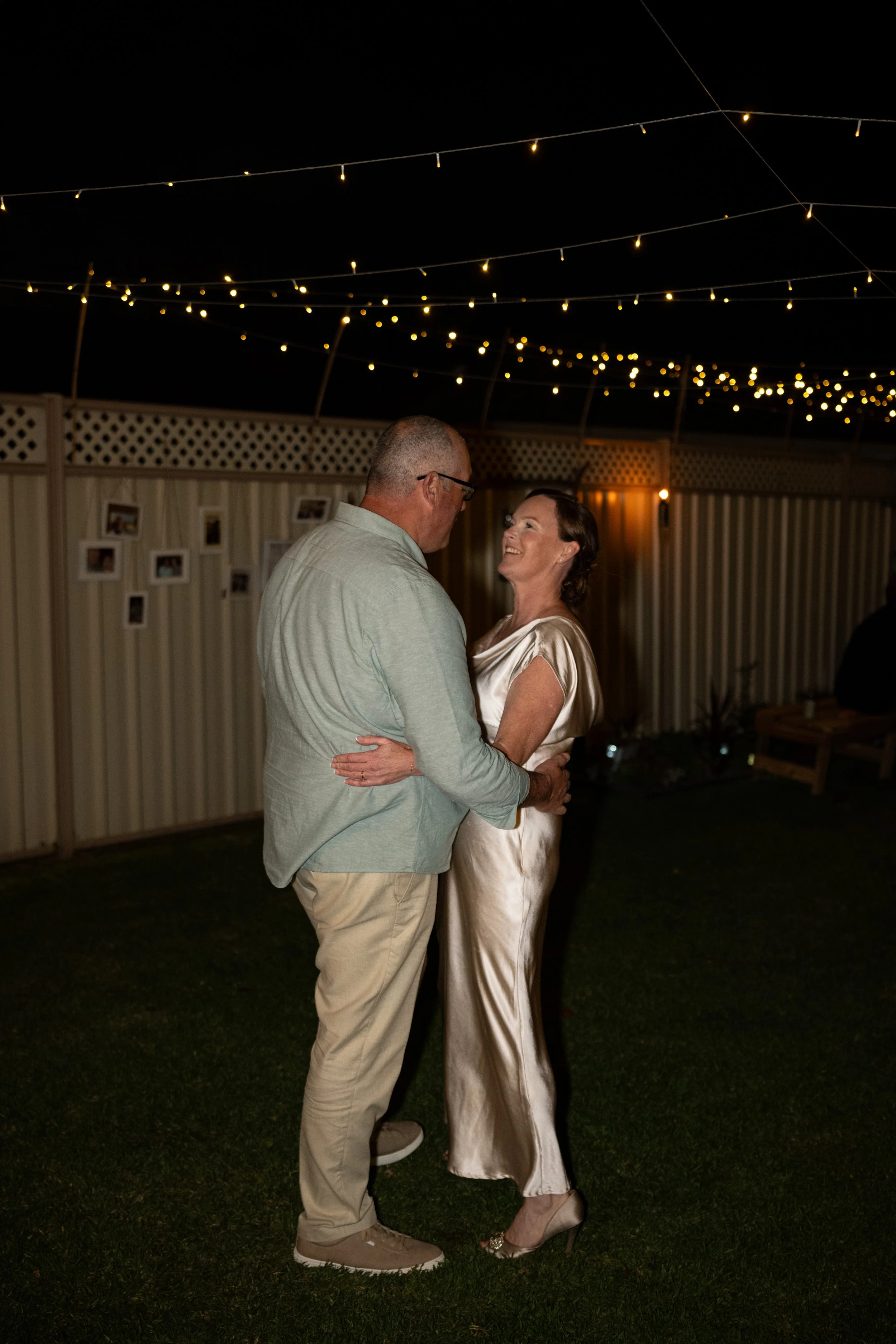 A couple dancing at an outdoor evening event with string lights overhead.