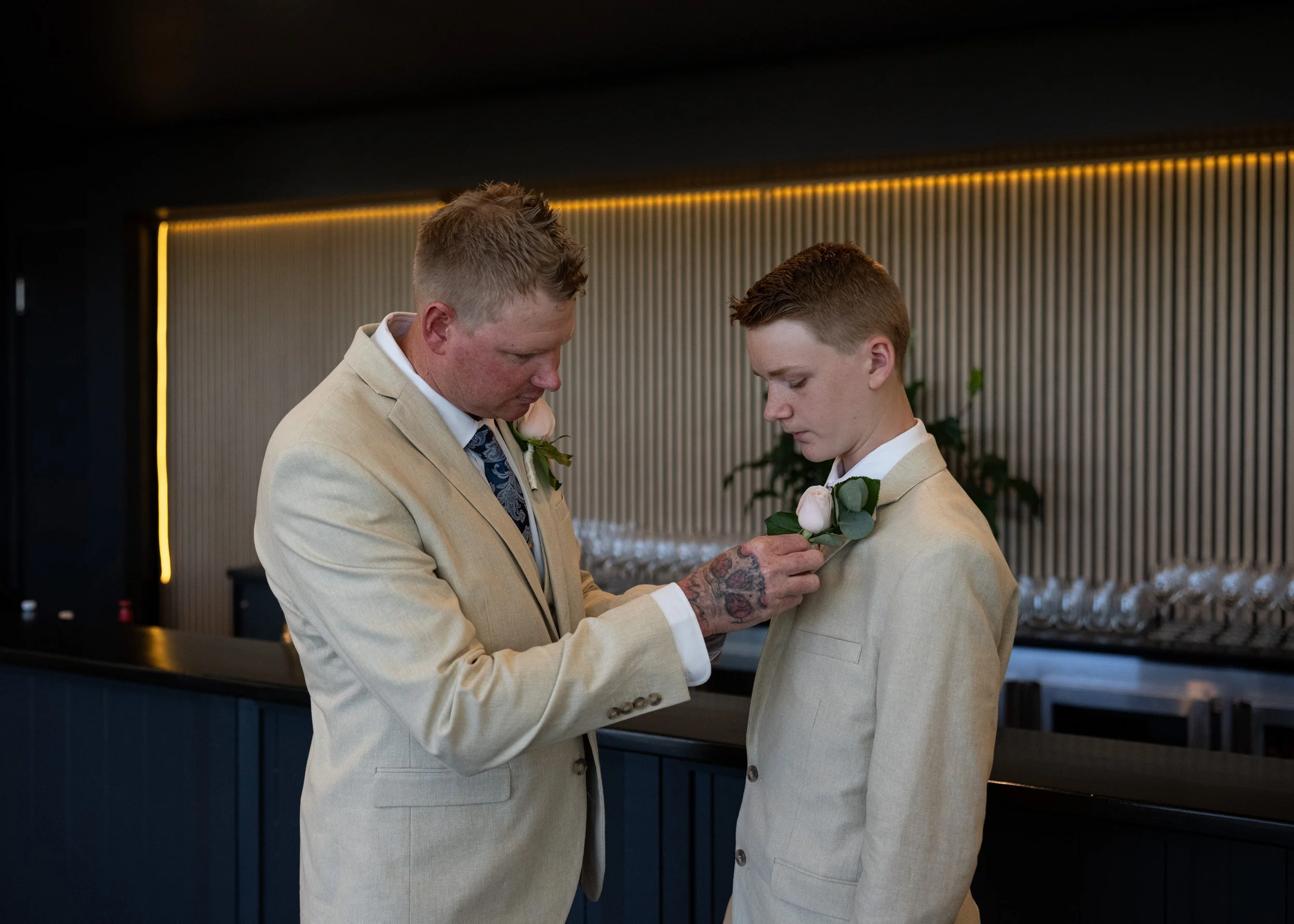 A man pinning a boutonniere on a young groom at a wedding in an indoor venue.