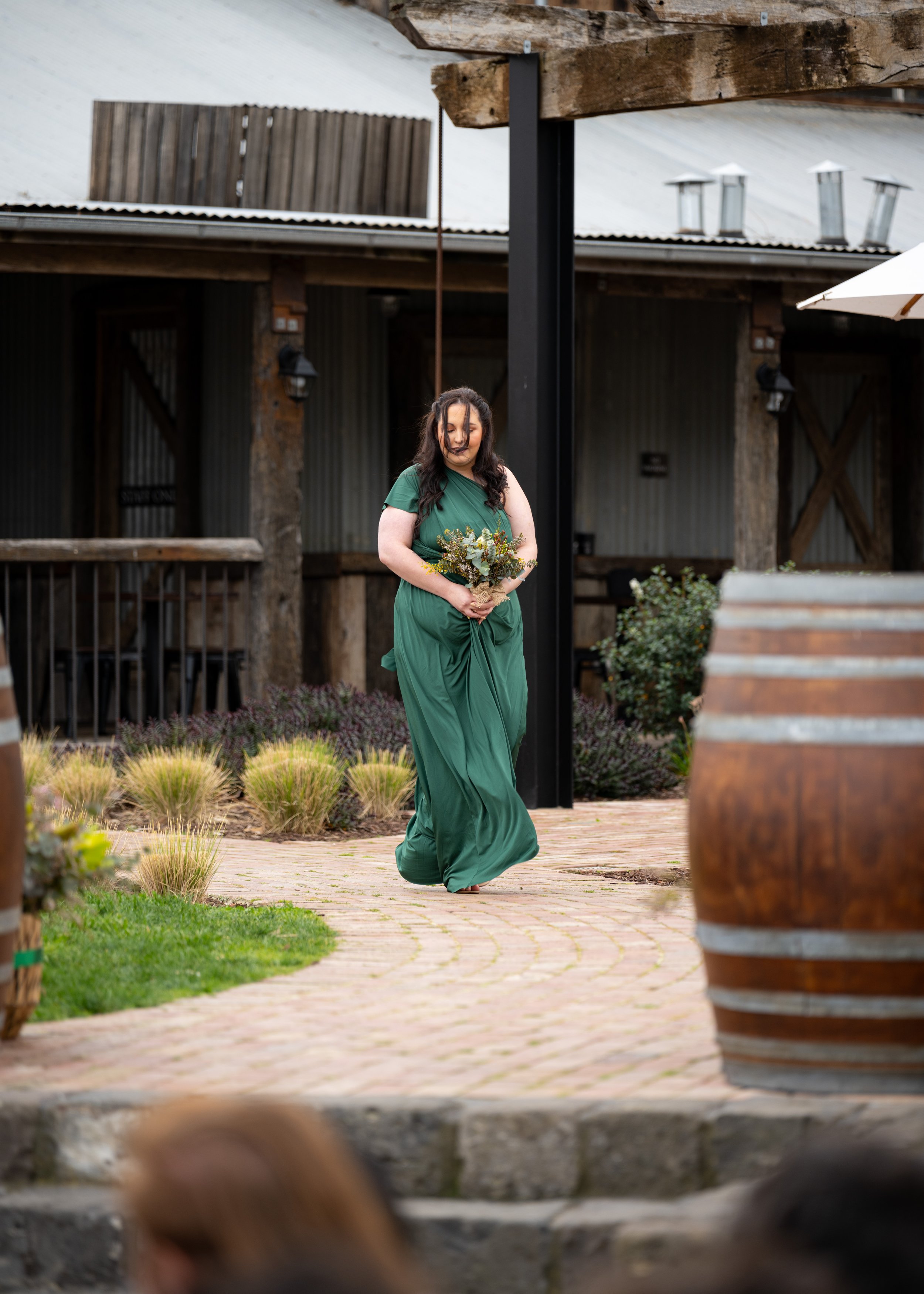A woman in a green dress holding a bouquet of flowers walking outdoors on a brick path