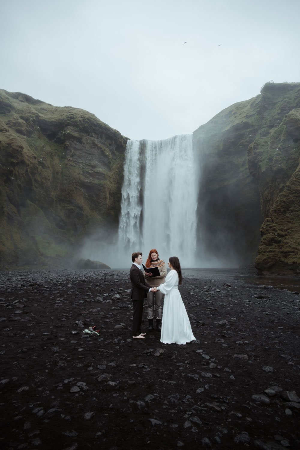 A couple exchanges vows during their intimate Iceland elopement ceremony beneath Skógafoss waterfall.