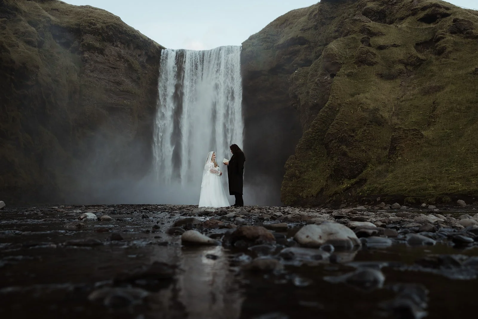 Hanna and Wyatt standing near the waterfall during their simple Iceland elopement