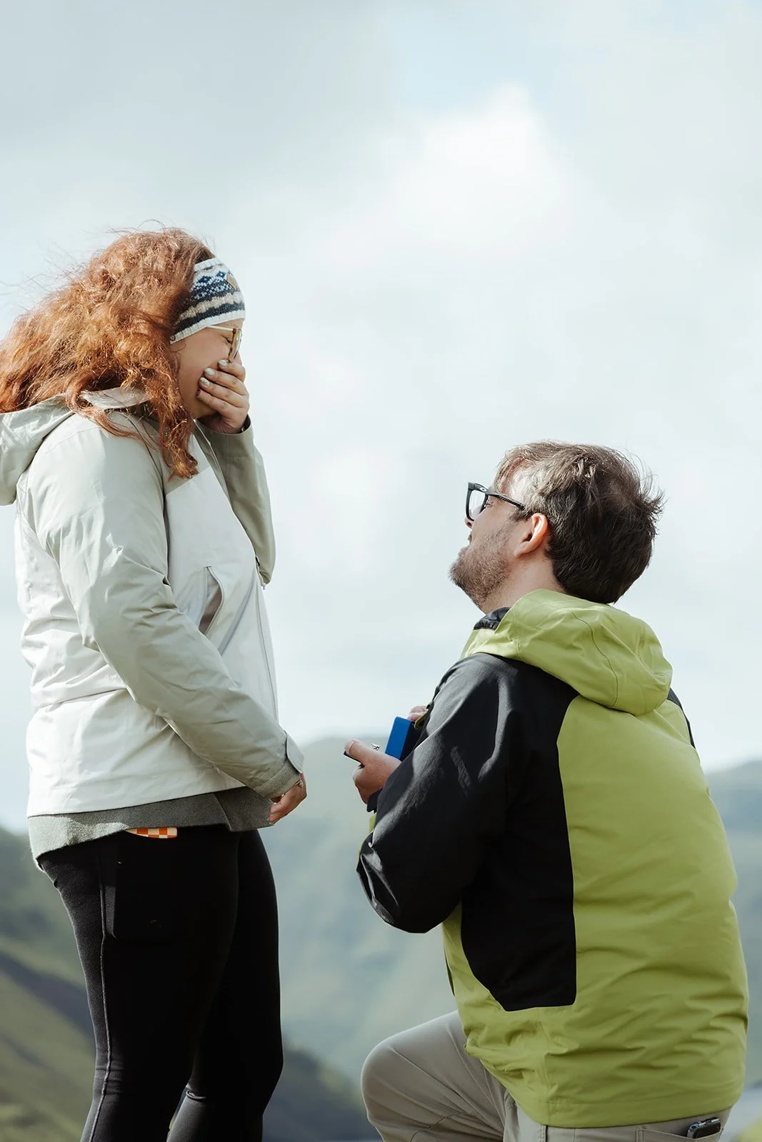 Hunter gets down on one knee as Natalie reacts to her surprise proposal in the Icelandic landscape.