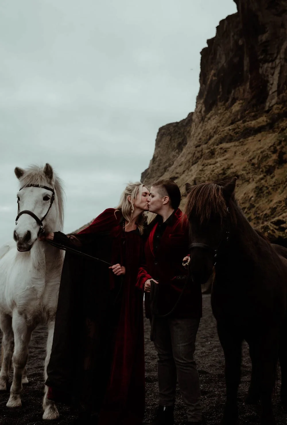 A couple kisses between two Icelandic horses during their personal Iceland elopement experience.