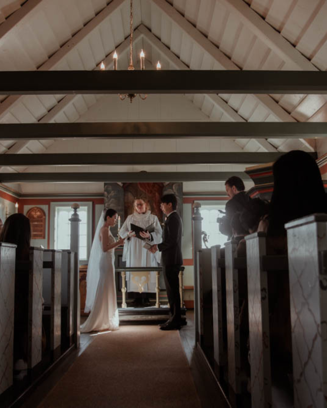 A couple stands before their officiant during an intimate wedding ceremony inside an Icelandic church.