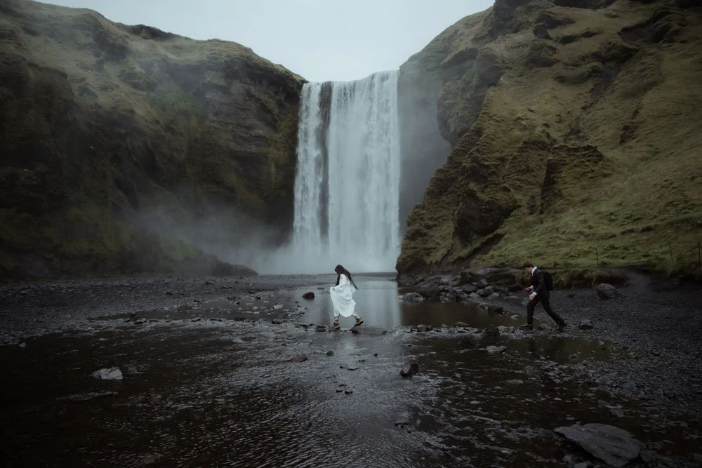 bride and groom walking across a river for their ceremony at Skogafoss
