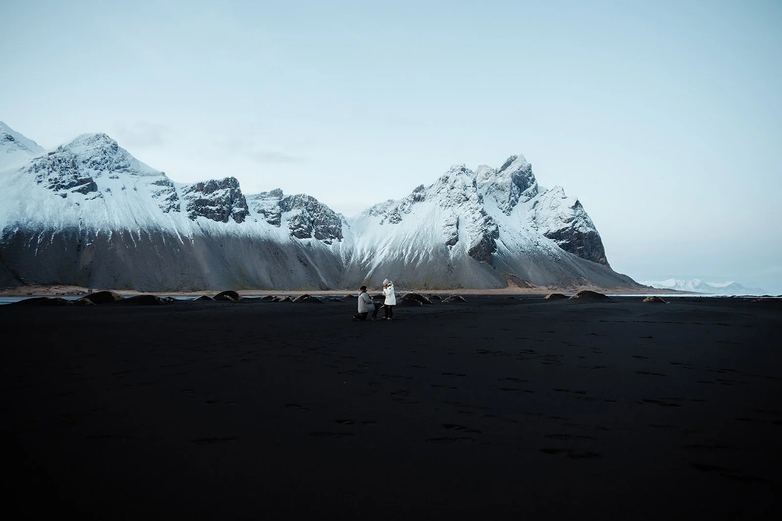 Couple celebrating a romantic proposal on Stokksnes black sand beach beneath Vestrahorn mountain in Iceland
