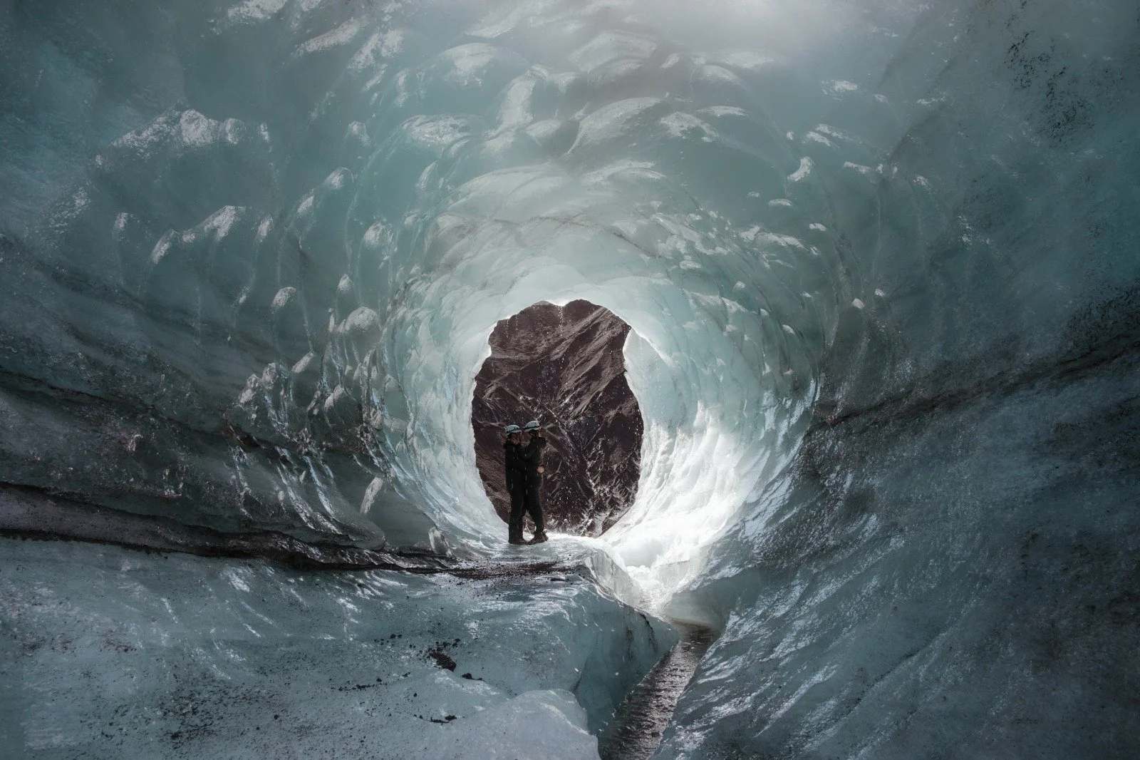 A couple stands together inside a blue ice cave during their private proposal experience in Iceland.