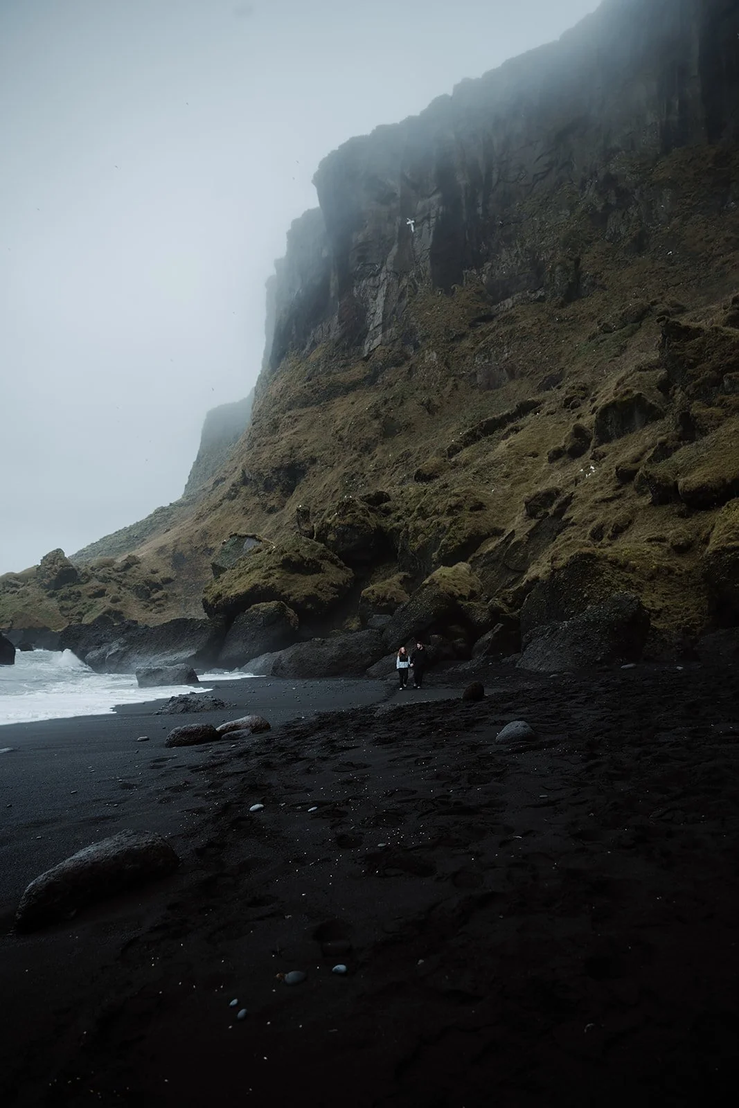 couple walking on black sand beach after engagement