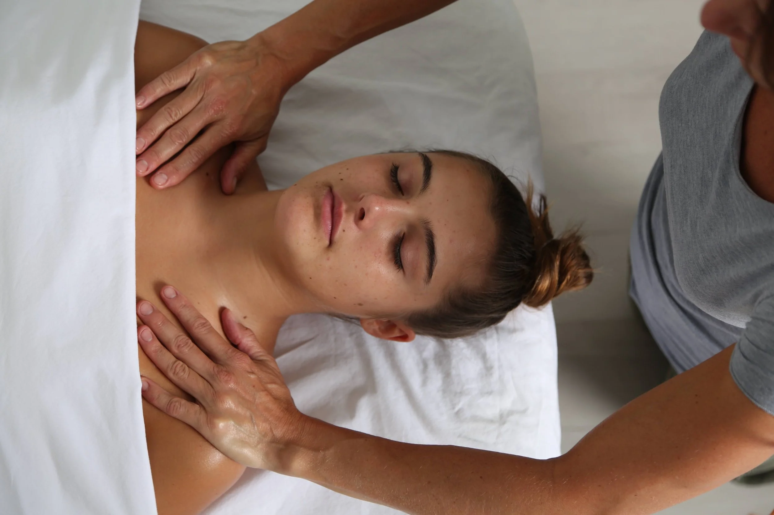 Image of a person receiving a blended session. The practitioner's hands are on her shoulders.