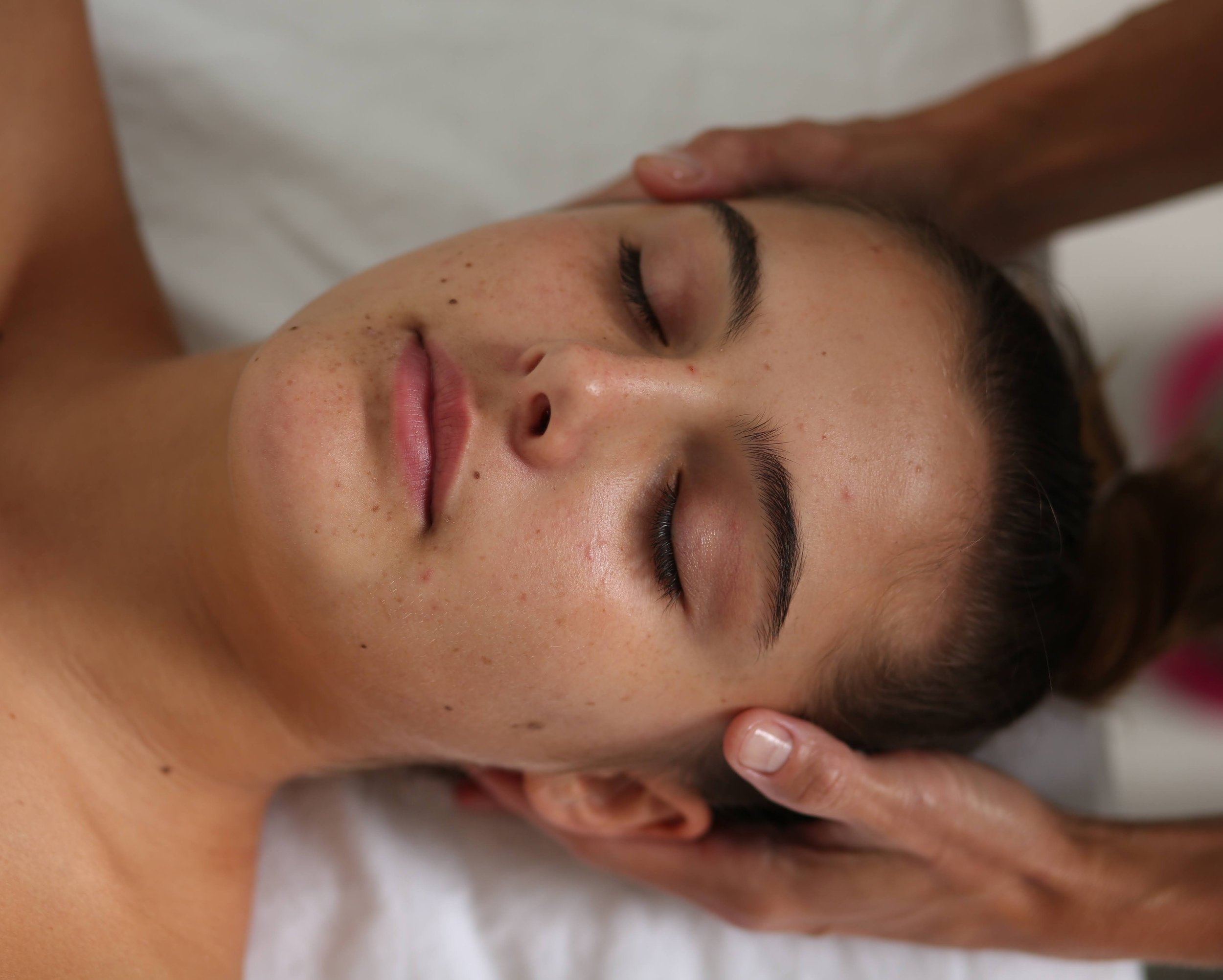 Photo of woman receiving craniosacral therapy. Practitioners hands are on the sides of her head.
