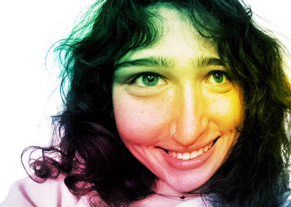 A woman with curly dark hair and green eyes smiling at the camera with rainbow filter overlay.
