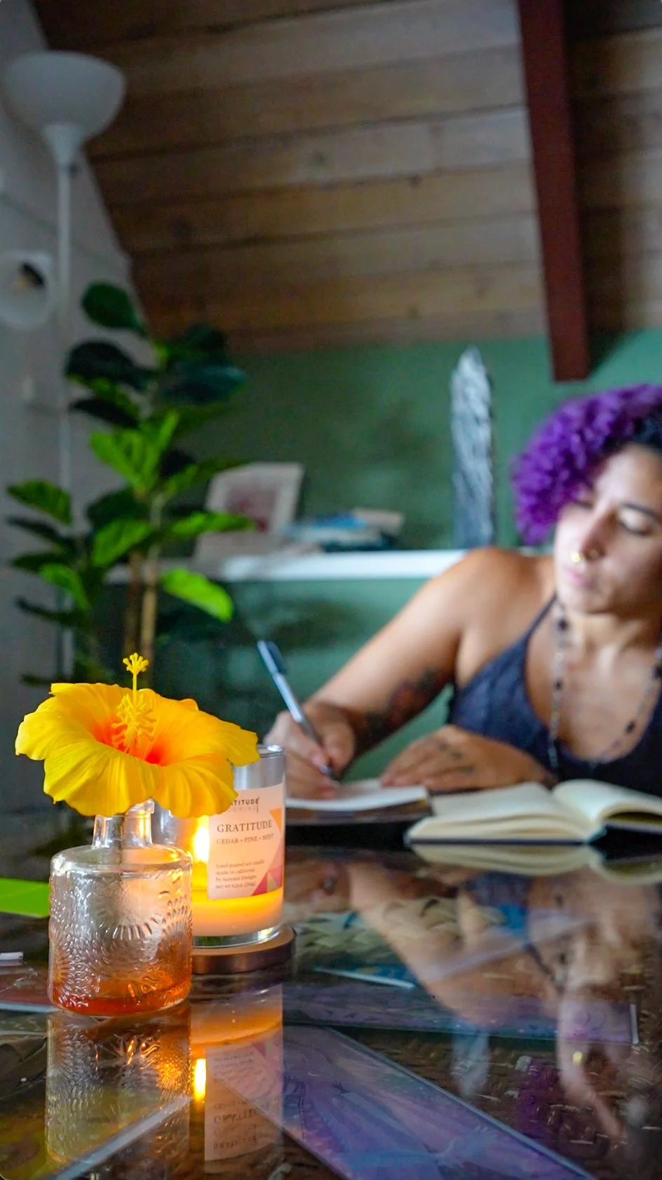  Woman writing in a journal at a candlelit table with a yellow hibiscus during a writers retreat 