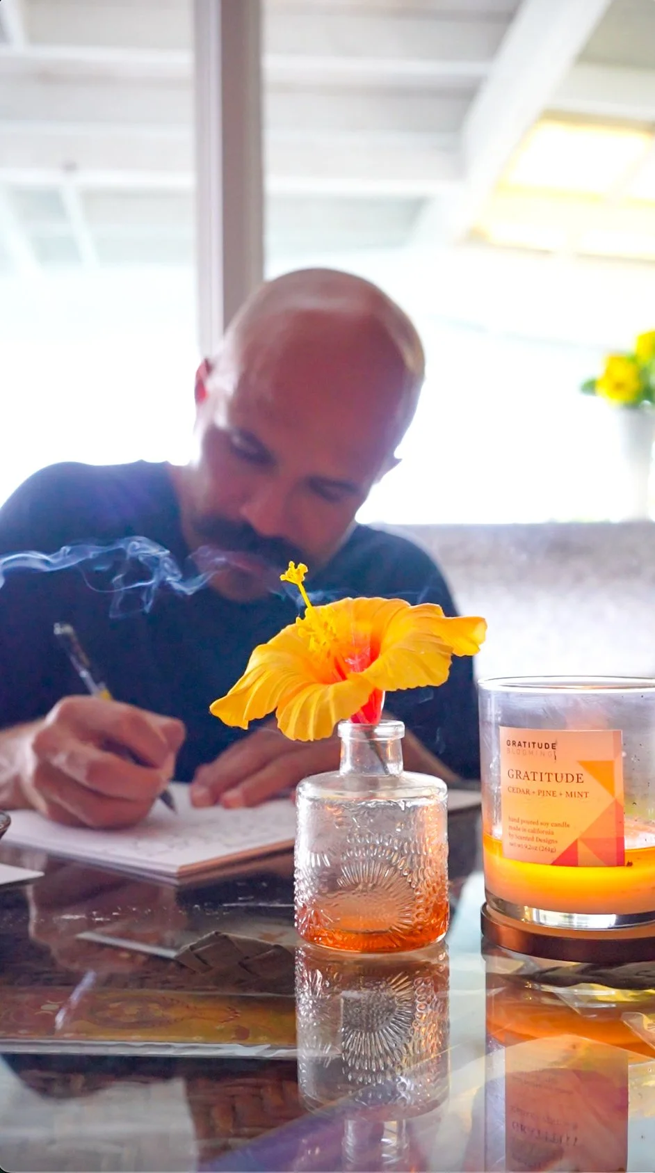  Man writing in a notebook beside burning incense and a yellow hibiscus during a writers retreat 