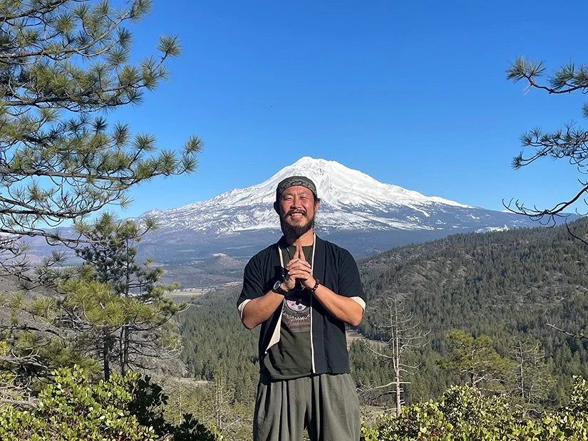  Smiling guest with hands in prayer pose in front of snow-capped Mount Shasta, California, on a retreat 