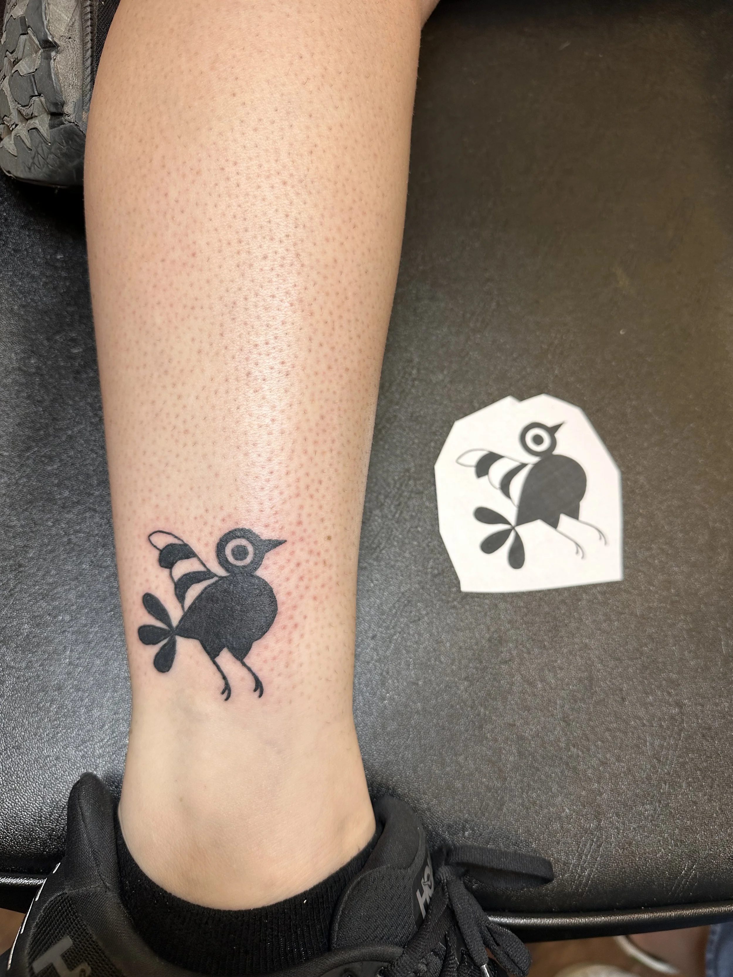 A small all-black stylized Bird tattoo