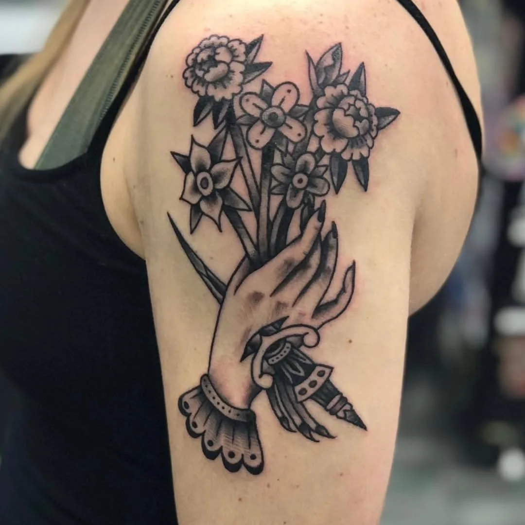 Zack recently tattooed this stunning, ornate piece for a client. This design features a delicate hand, complete with an intricate lace-like cuff around the wrist, being pierced through by a beautifully detailed dagger. The hand is shown clutching a l