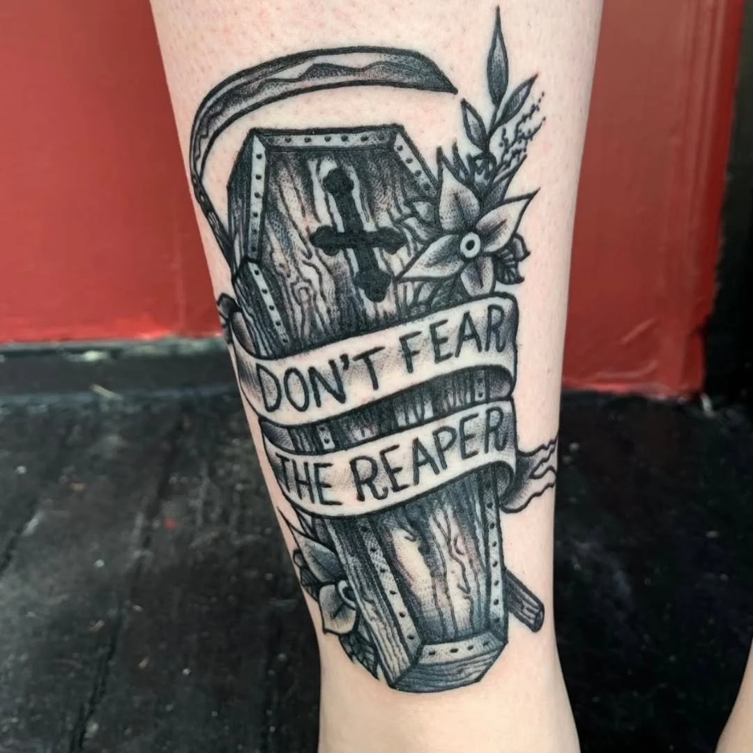 Zack recently inked this sick stylized neo-traditional blackwork coffin, replete with rich wood grain! Emblazoned with an inverted cross and surrounded by burial flowers, the piece is wrapped in a banner that clearly reads, "Don't Fear the Reape