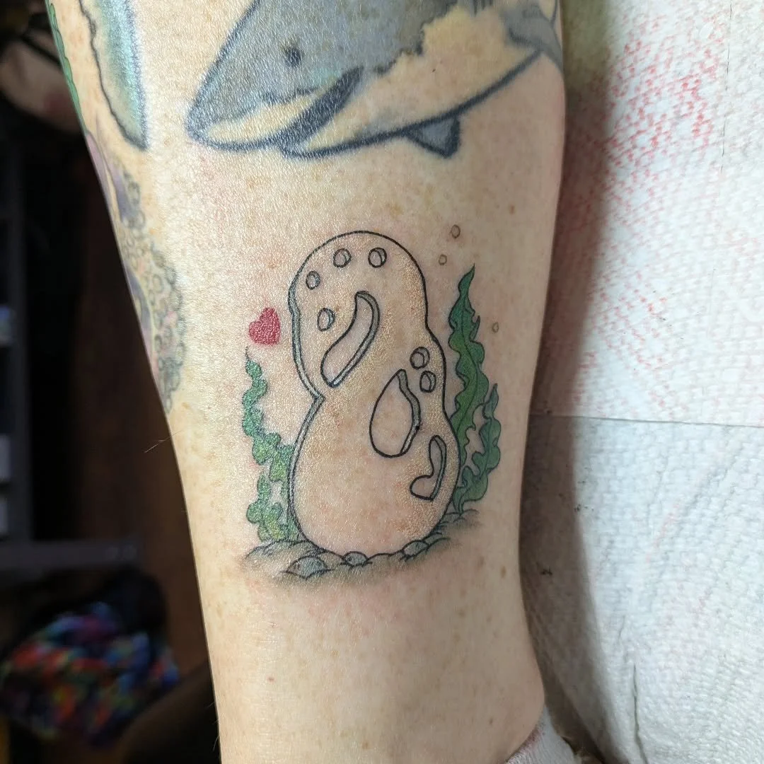 Rachel recently tattooed this meaningful memorial piece of a Polynesian pendant. The design rests on the ocean floor among swaying seaweed and small stones, featuring a tiny red heart for a soft, personal touch. It&rsquo;s a wonderful way to carry a 