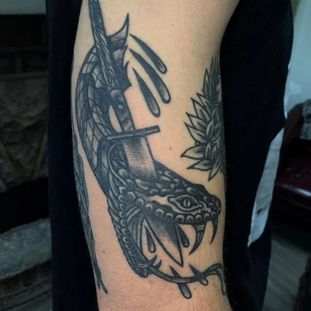 Zack inked this fierce traditional blackwork viper. The tattoo features a detailed viper head, fangs exposed, with a speartip driving clean through it. Heavy black shading creates incredible depth, perfectly capturing the intensity of the scene. 🛡️?