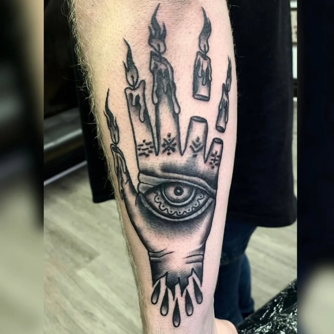 Check out this striking piece by Zack, a traditional blackwork hand with detailed fingers, each transformed into a lit, melting wax candle and adorned with a sigil. The back of the hand features a prominent open eye, bringing the entire design togeth