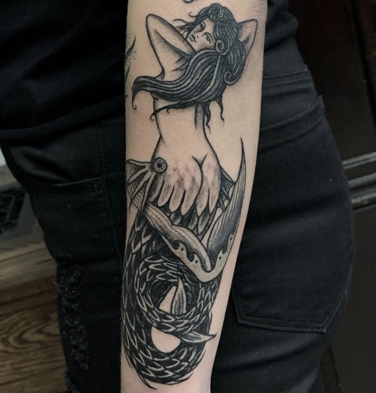 Blackwork tattoo of a playful mermaid on a forearm.
