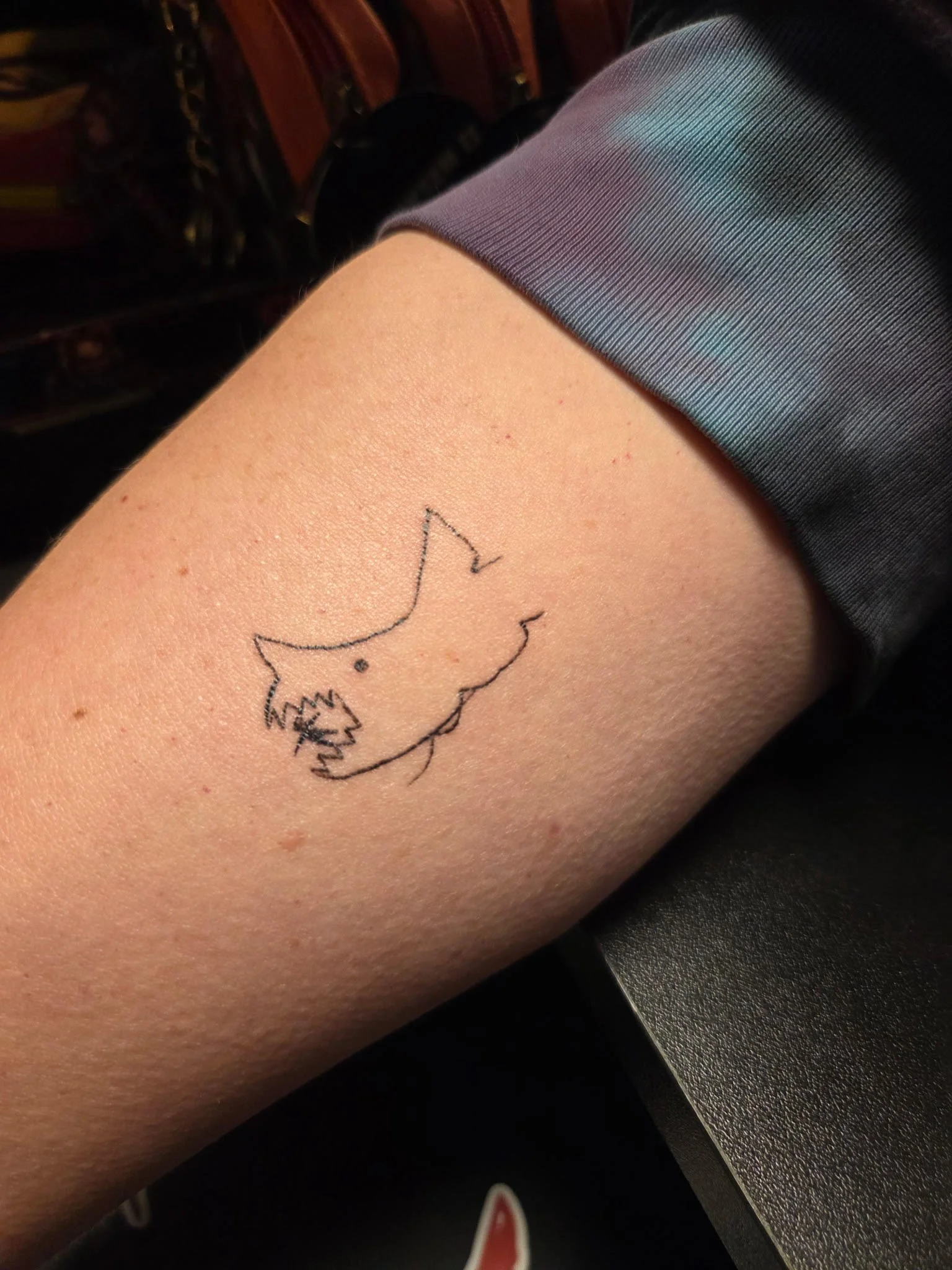 A line tattoo of a shark swallowing a swimming victim. 