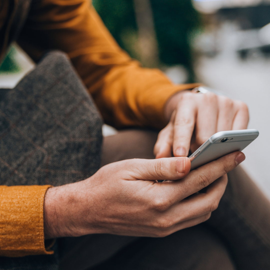 Close-up of a person holding and using a smartphone, with focus on hands and phone, outdoors setting.