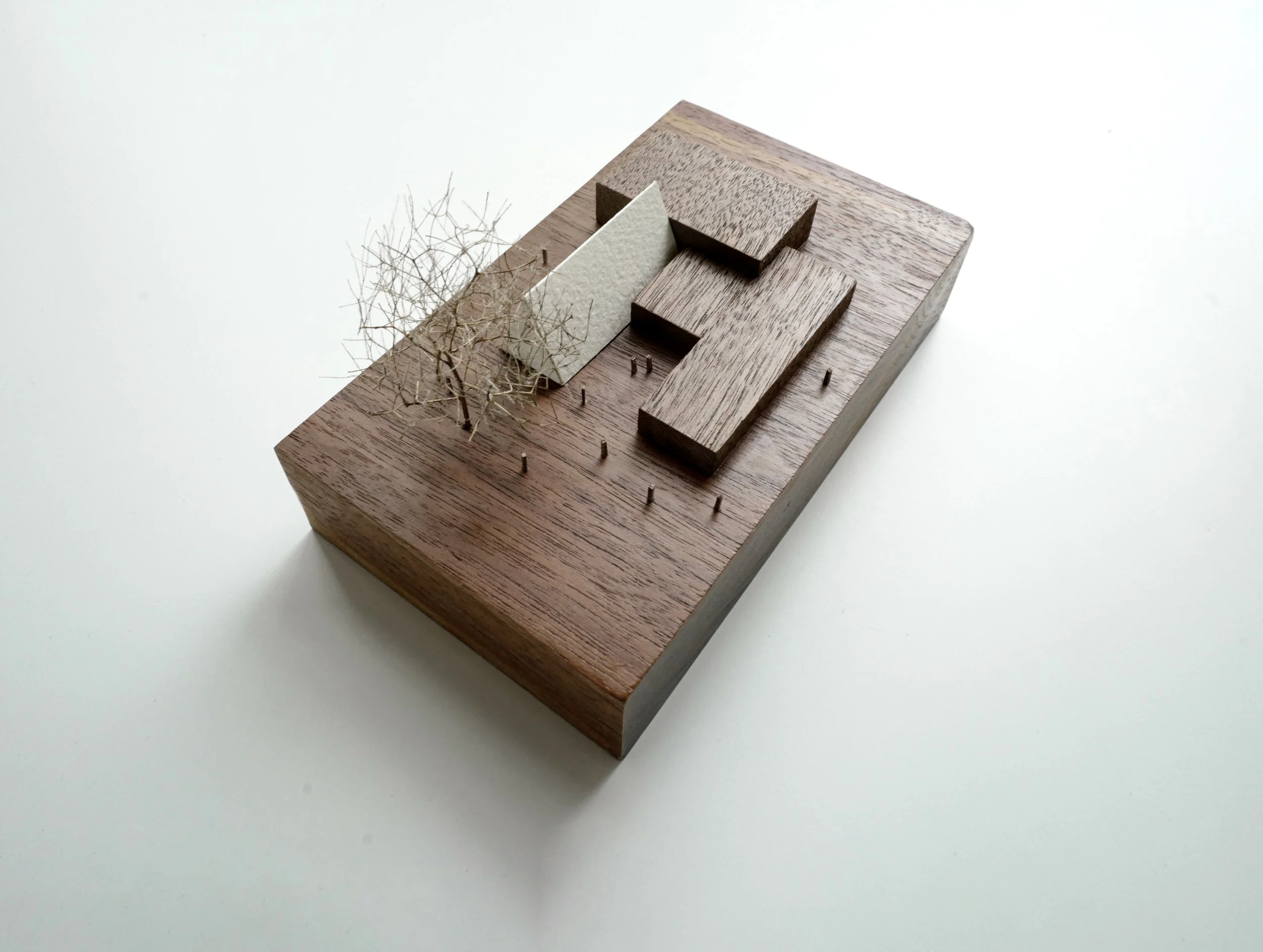 Modello di architettura in miniatura con un edificio in legno, uno spazio con piccoli alberi e una superficie di base in legno.