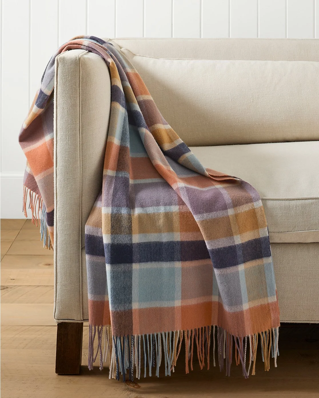A plaid blanket draped over the arm of a beige sofa in a cozy living room.
