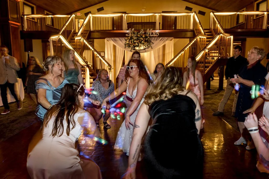 People dancing at a wedding reception with a wooden two-story building in the background decorated with string lights and floral arrangements.