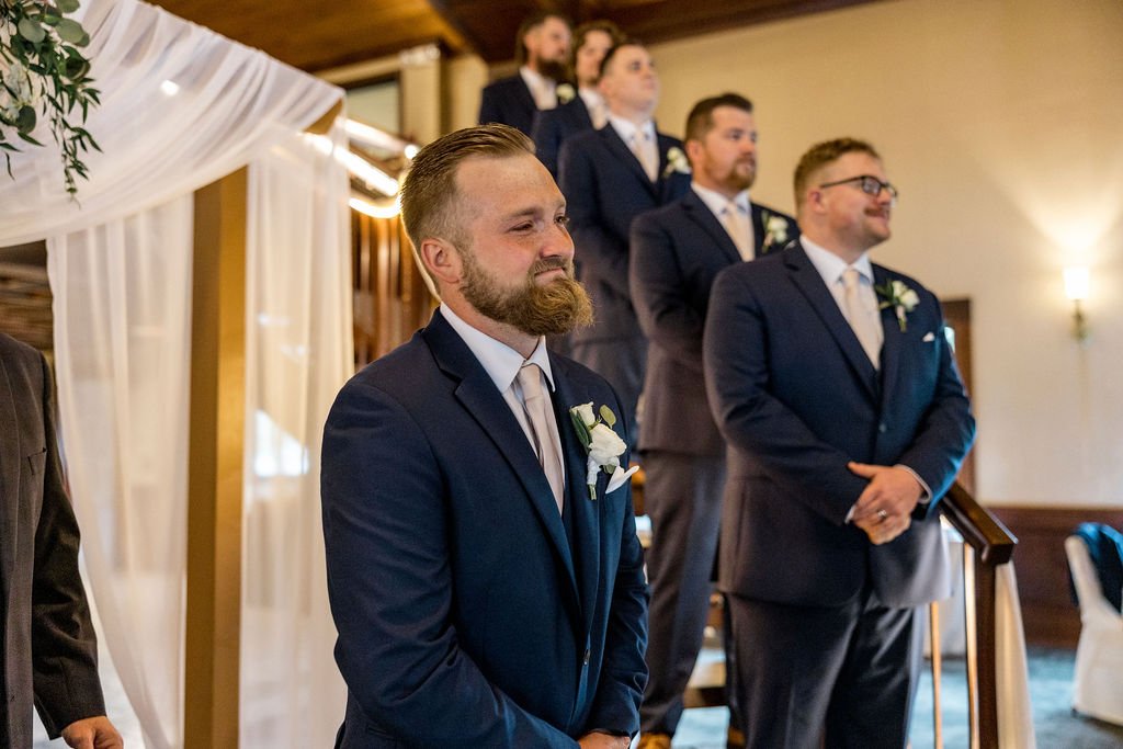Groom and groomsmen at a wedding in formal suits, standing in a decorated indoor venue.