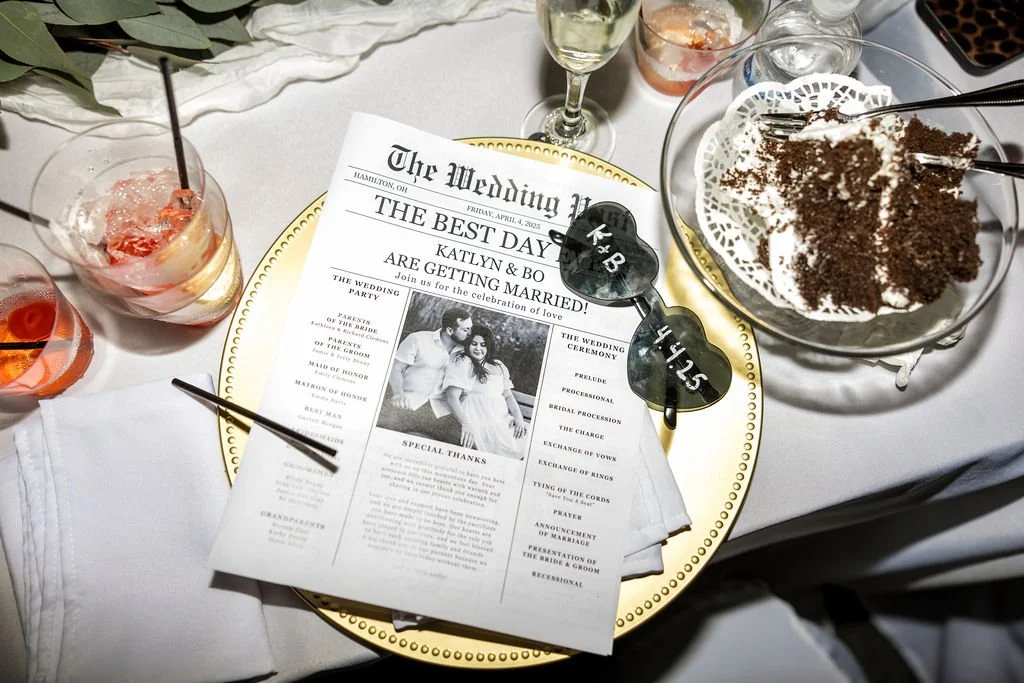 Wedding reception table with a program, glasses of drinks, sunglasses, and a dessert with chocolate.