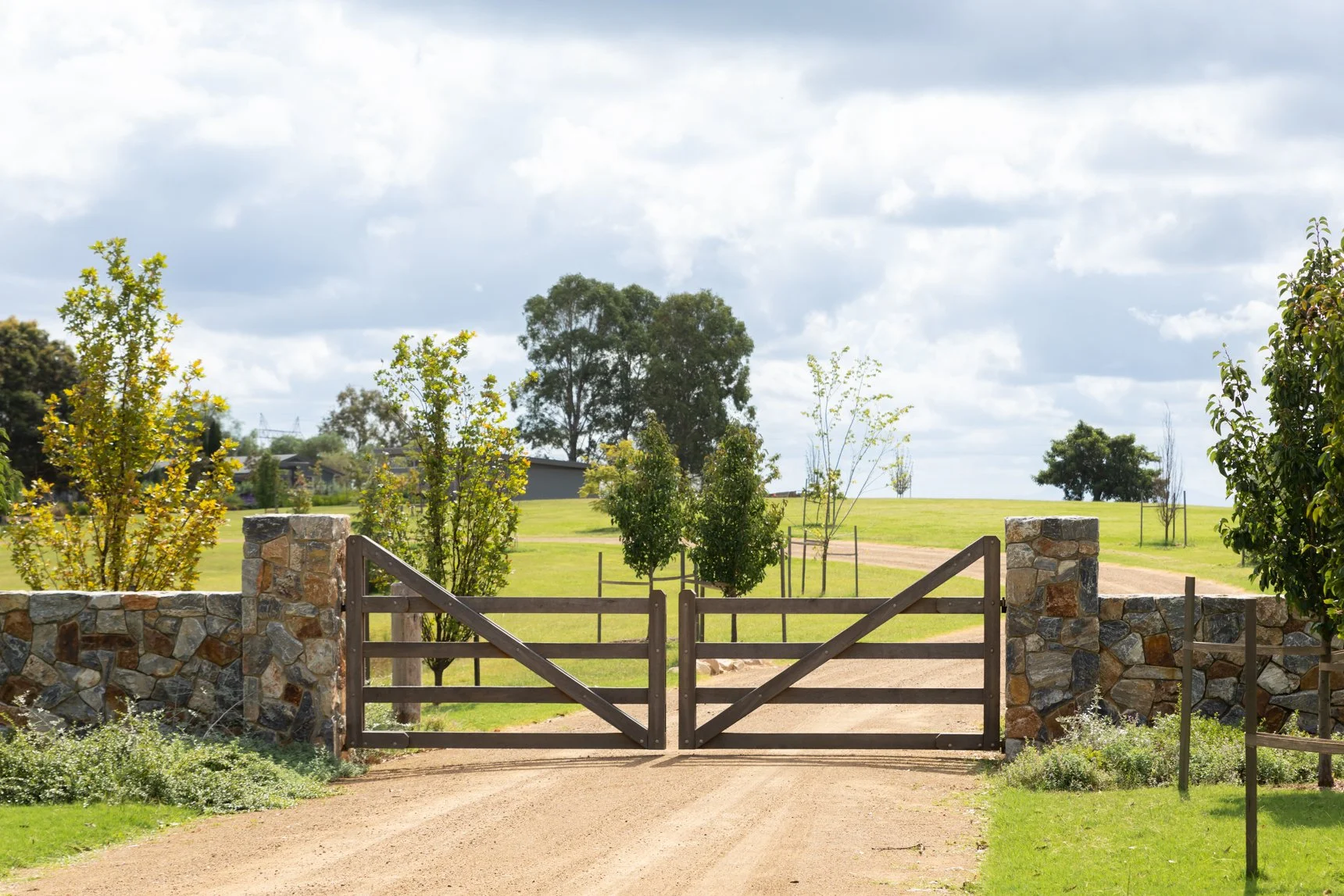 Newcastle builder wooden gate with stone pillars leading to grassy field.