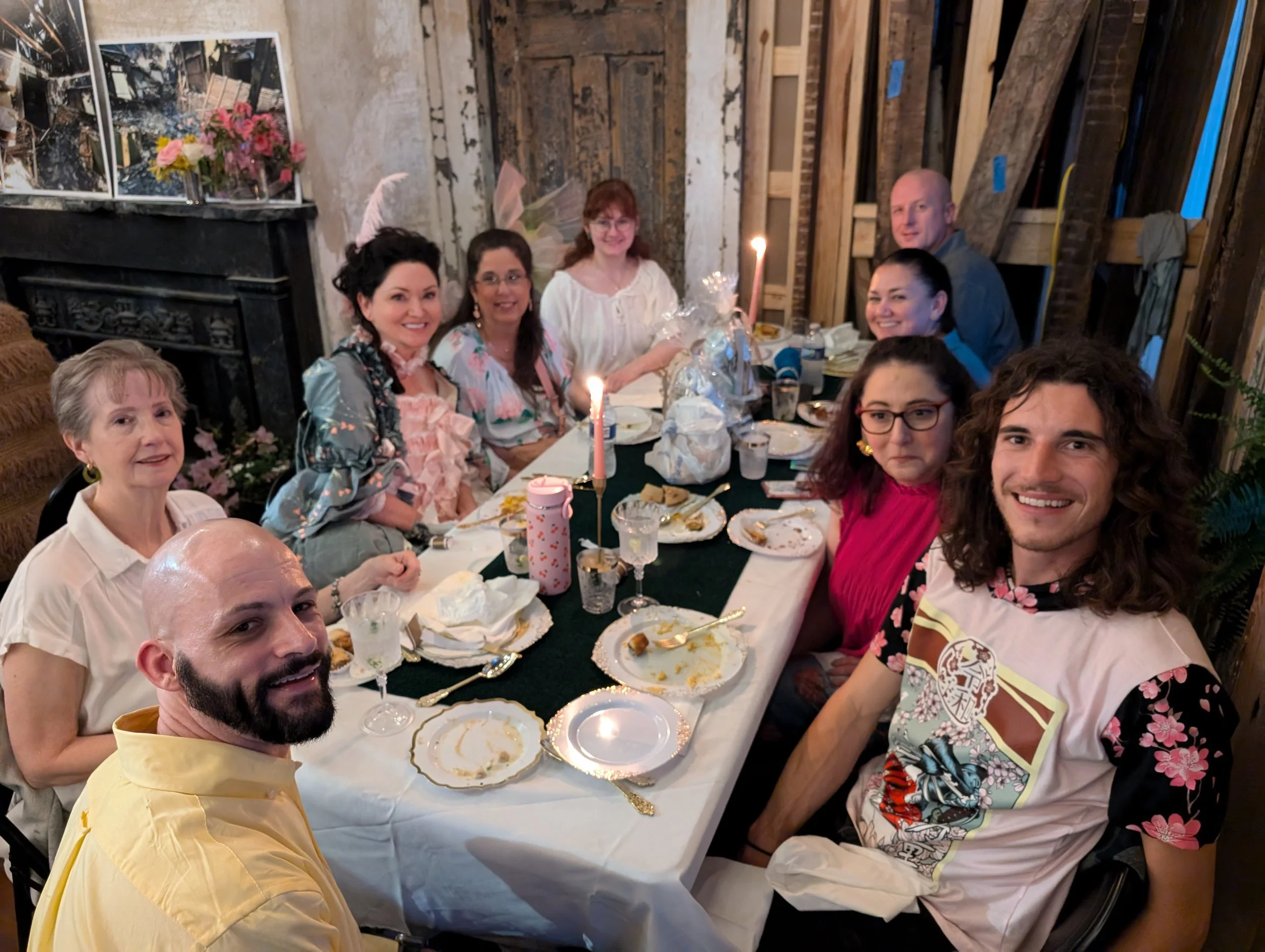 A group of people gathered around a decorated birthday dinner table, celebrating with laps and gifts, some with bunny ear headbands, and birthday candles on the table.