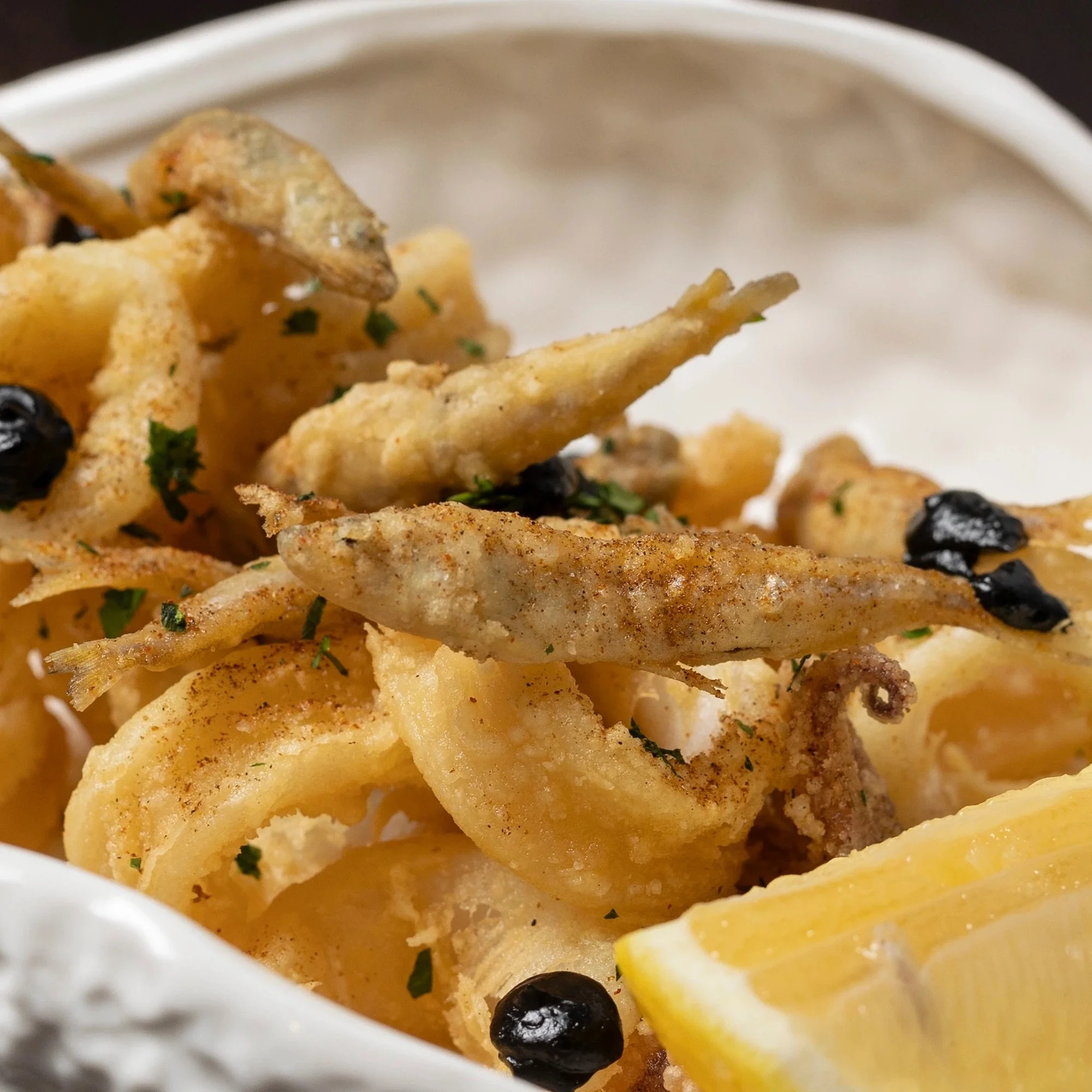 Close-up of fried calamari with lemon wedges and black pepper in a white bowl