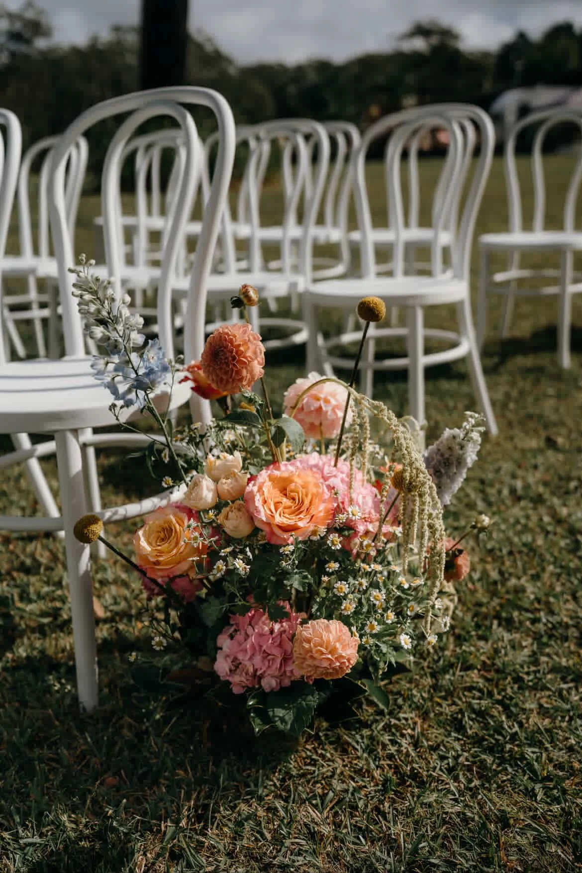 Flowers in a basket in front of white chairs outdoors during daytime.